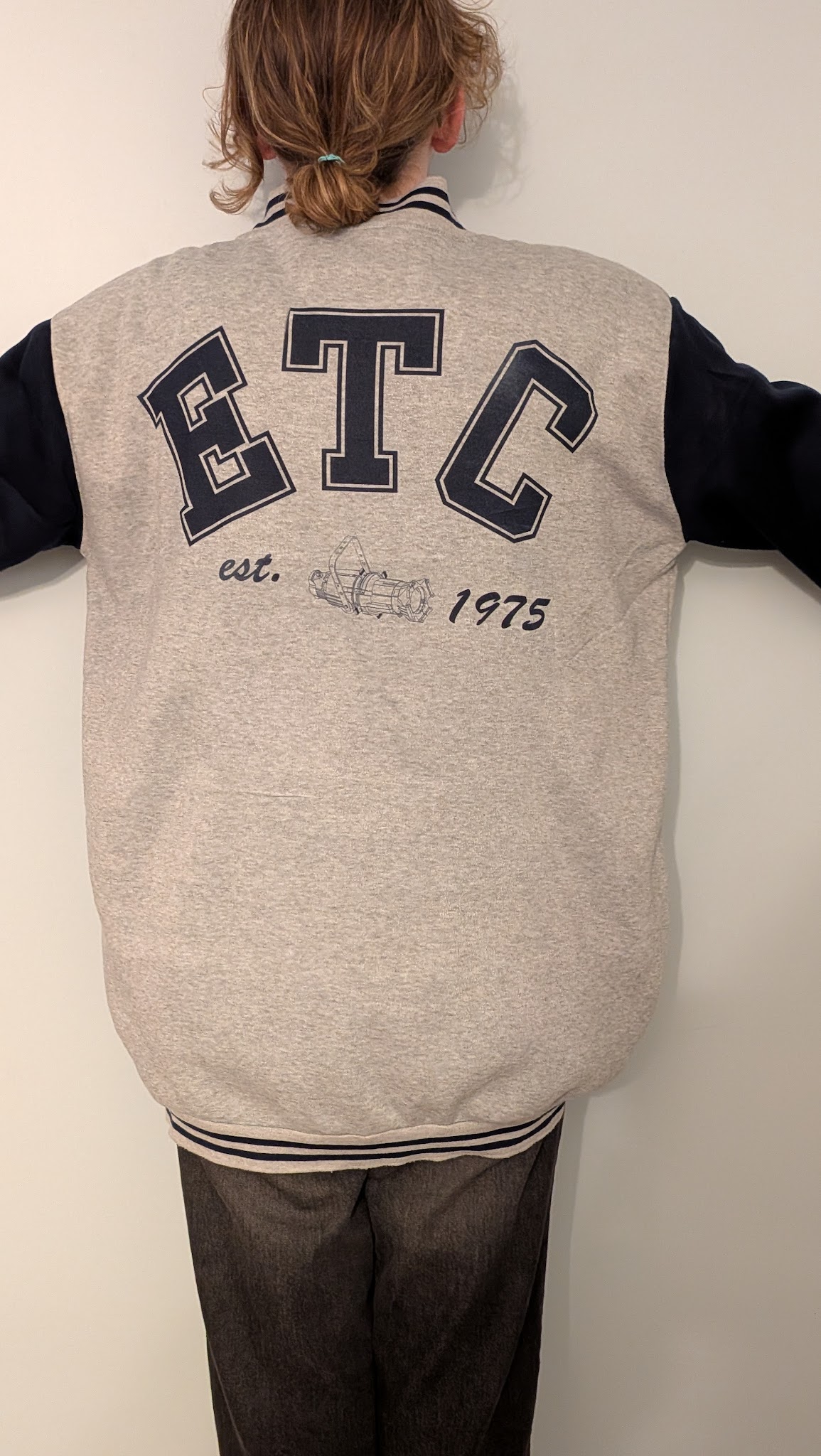 The back of a varsity jacket. The Letters ETC are spelled out, above a moving light, which has 'est. 1975' to the sides.
